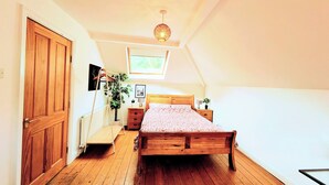 A bedroom with a wooden bed, a wooden dresser, a nightstand, a hanging plant, and a skylight.