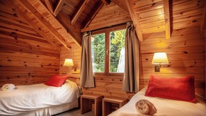 Acogedora habitación tipo cabaña con dos camas, paredes de madera y una ventana con cortinas.
