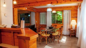 Interior de una cabaña de madera con comedor, mostrador de cocina y sala de estar.