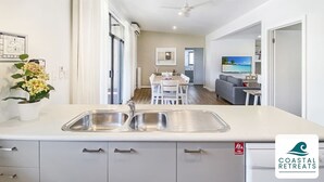 A modern kitchen with a central island, a dining area with a table and chairs, and a living room with a sofa and TV. - 🏝 Luxury Poolside Retreat – Ramada Resort (Cowes)
