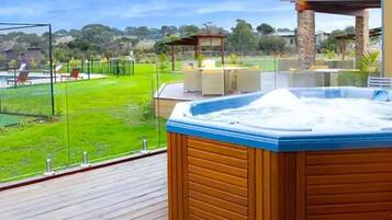 A hot tub on a wooden deck with a view of a grassy area and a gazebo.