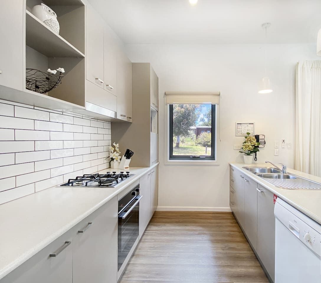 Een moderne keuken met witte kasten, een gasfornuis en een raam met uitzicht op de omgeving.