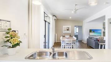 Une cuisine moderne avec un îlot central, un coin repas avec une table et des chaises, et un salon avec un canapé et une télévision.