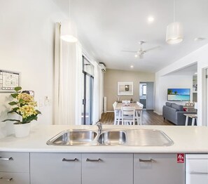 Une cuisine moderne avec un îlot central, un coin repas avec une table et des chaises, et un salon avec un canapé et une télévision.