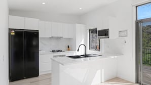 A modern kitchen with white cabinetry, a black refrigerator, a built-in microwave, and a large island with a sink. - Luxury Hills Retreat – Villa Ramada Resort (Cowes)