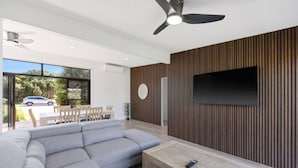A modern living room with a sectional sofa, a wooden coffee table, and a flat-screen TV mounted on a wooden wall. - Luxury Hills Retreat – Villa Ramada Resort (Cowes)