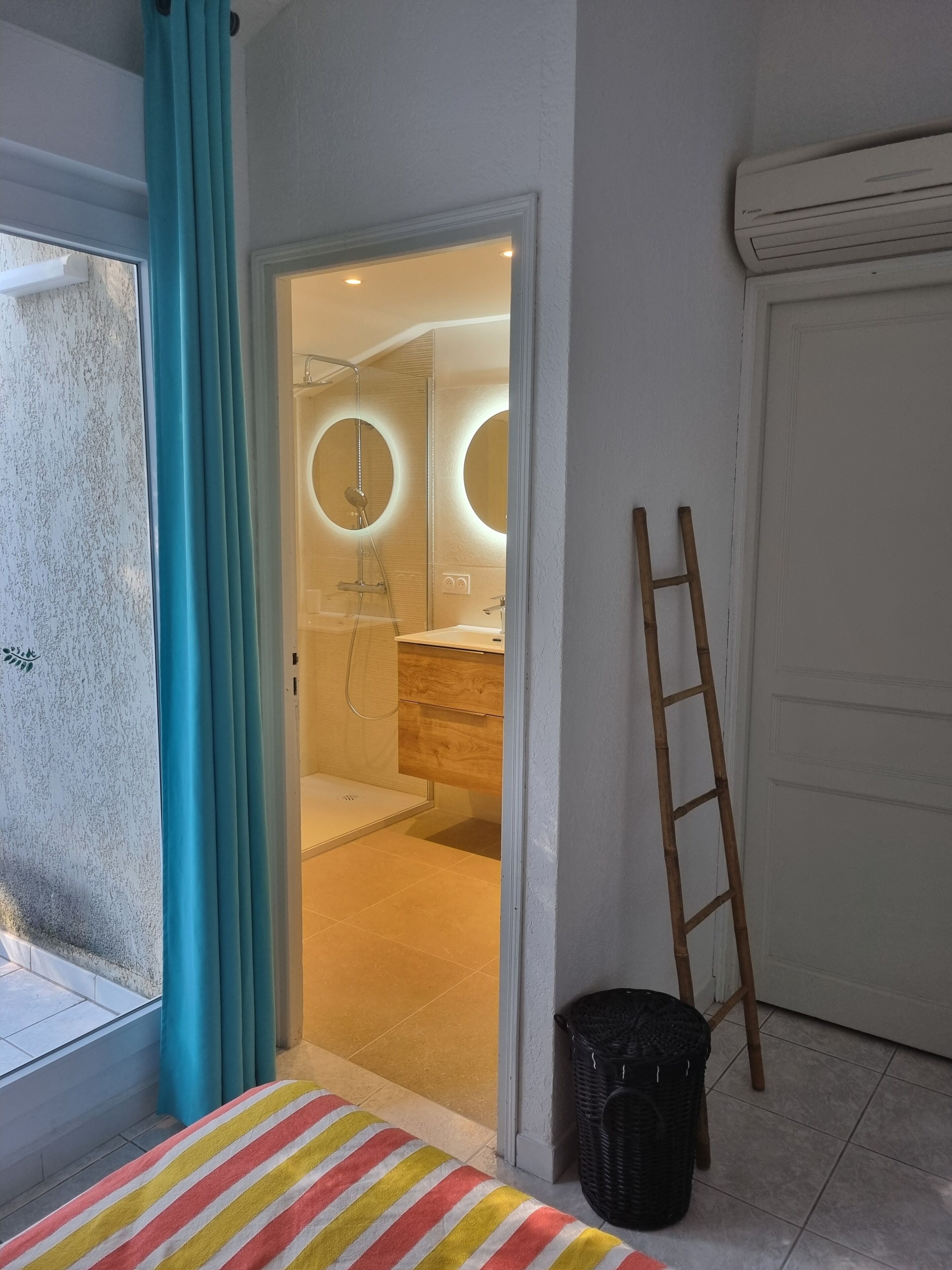 A room with a bed, a window with curtains, a door leading to a bathroom, and a wooden ladder.