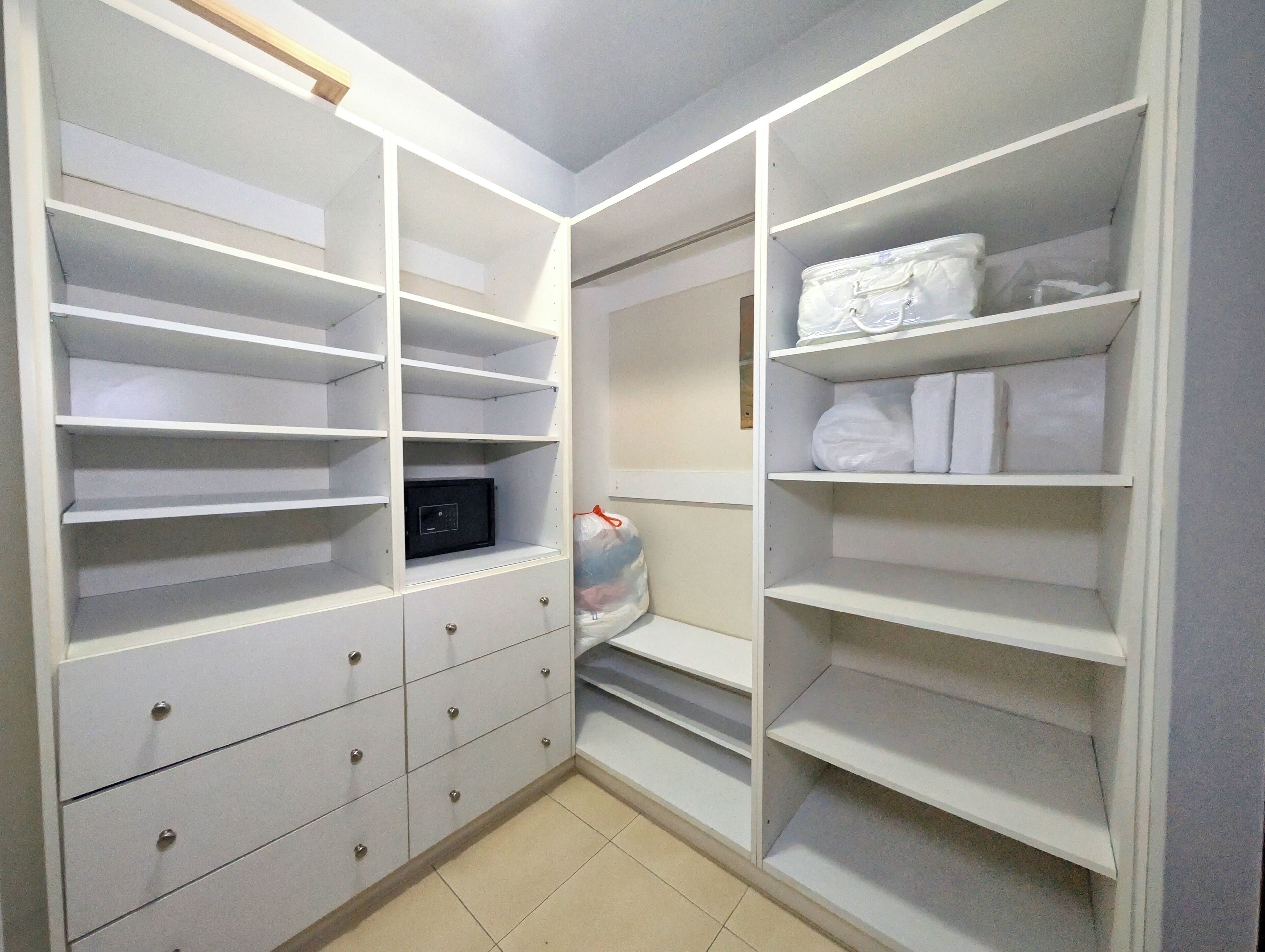 A walk-in closet with multiple shelves and drawers, a black electronic device on one shelf, and a plastic bag on the floor.