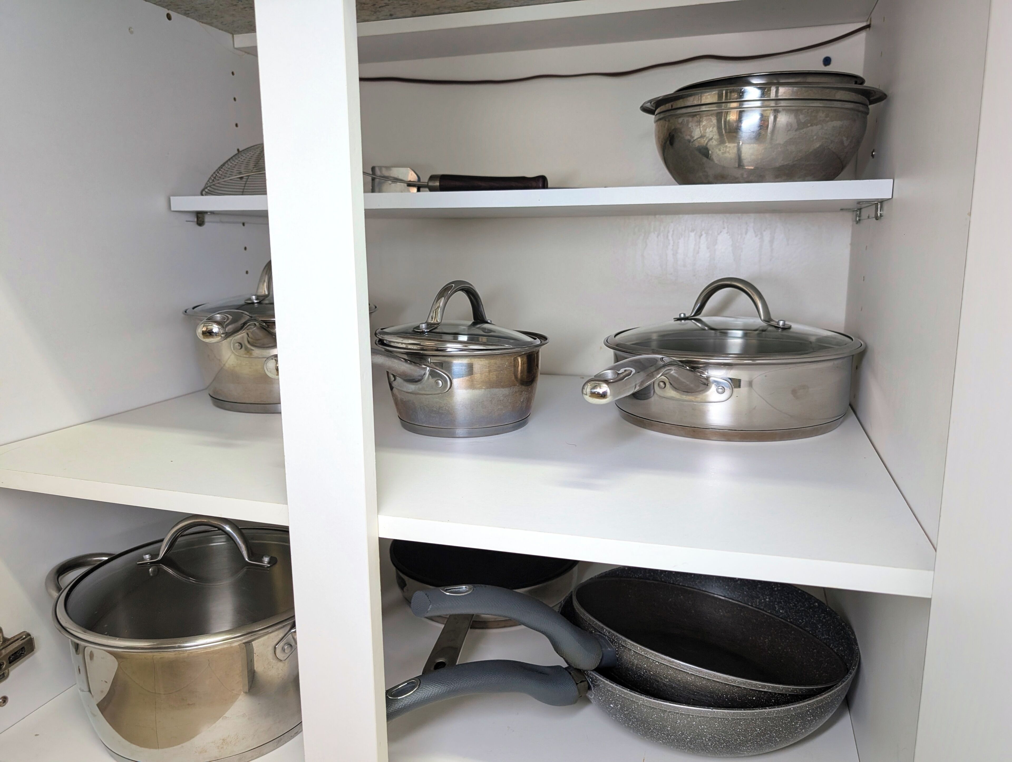 Una cocina con utensilios de acero inoxidable en estantes blancos, incluyendo ollas, sartenes y un rallador.