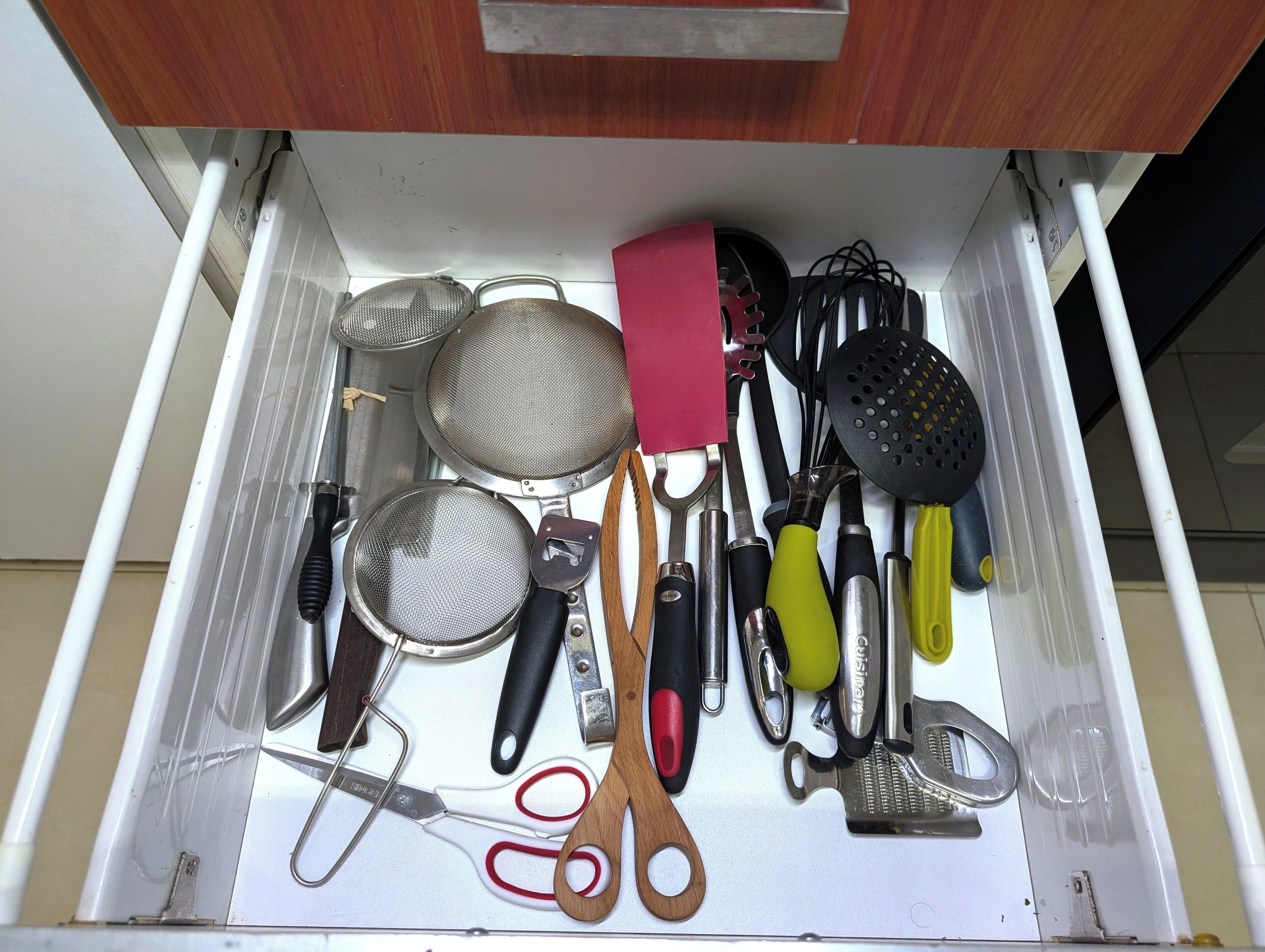 A drawer with kitchen utensils including a strainer, spatula, and various other tools.