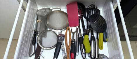 A drawer with kitchen utensils including a strainer, spatula, and various other tools.