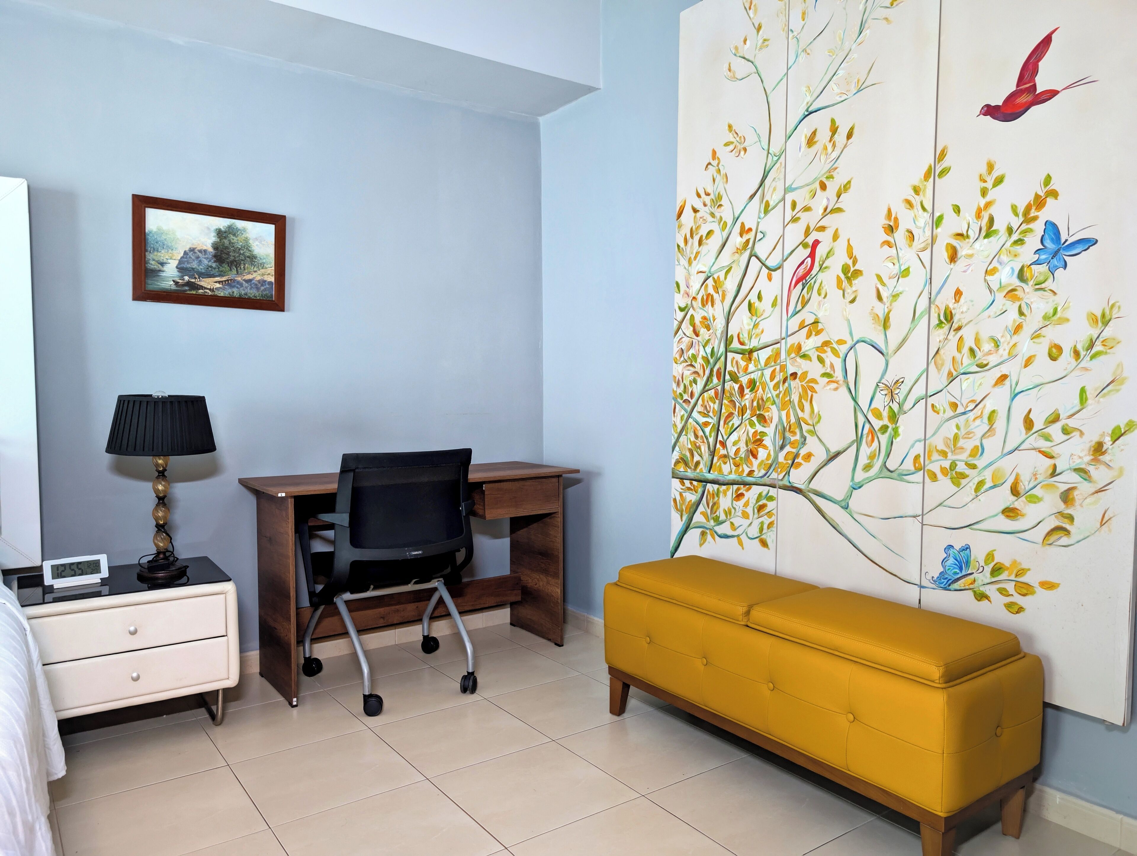Une pièce comprenant un bureau, une chaise, une table de chevet et un banc jaune.