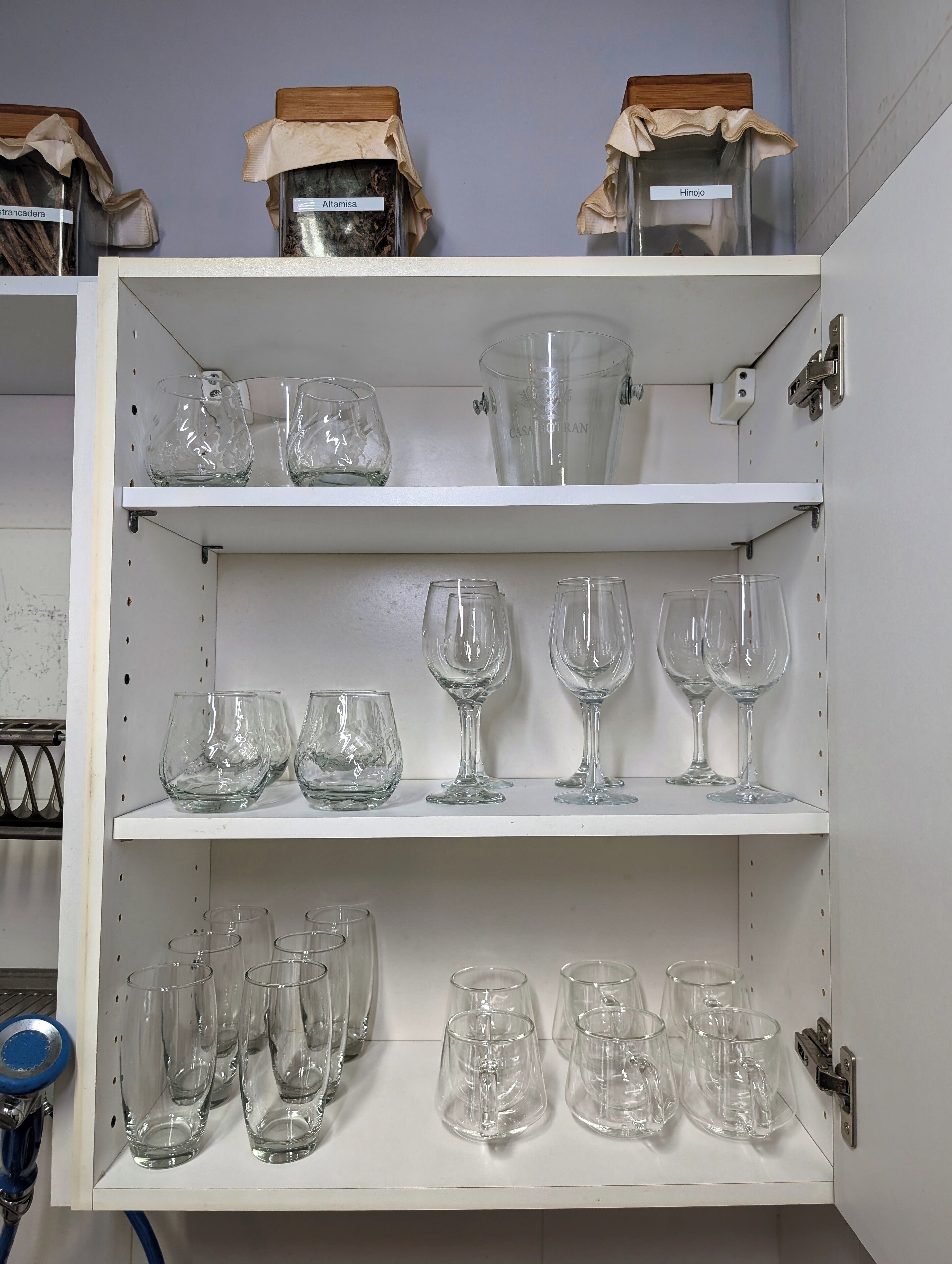 Un meuble de rangement doté d’étagères où sont rangés divers types de verrerie, notamment des verres à vin et des verres à cocktail.