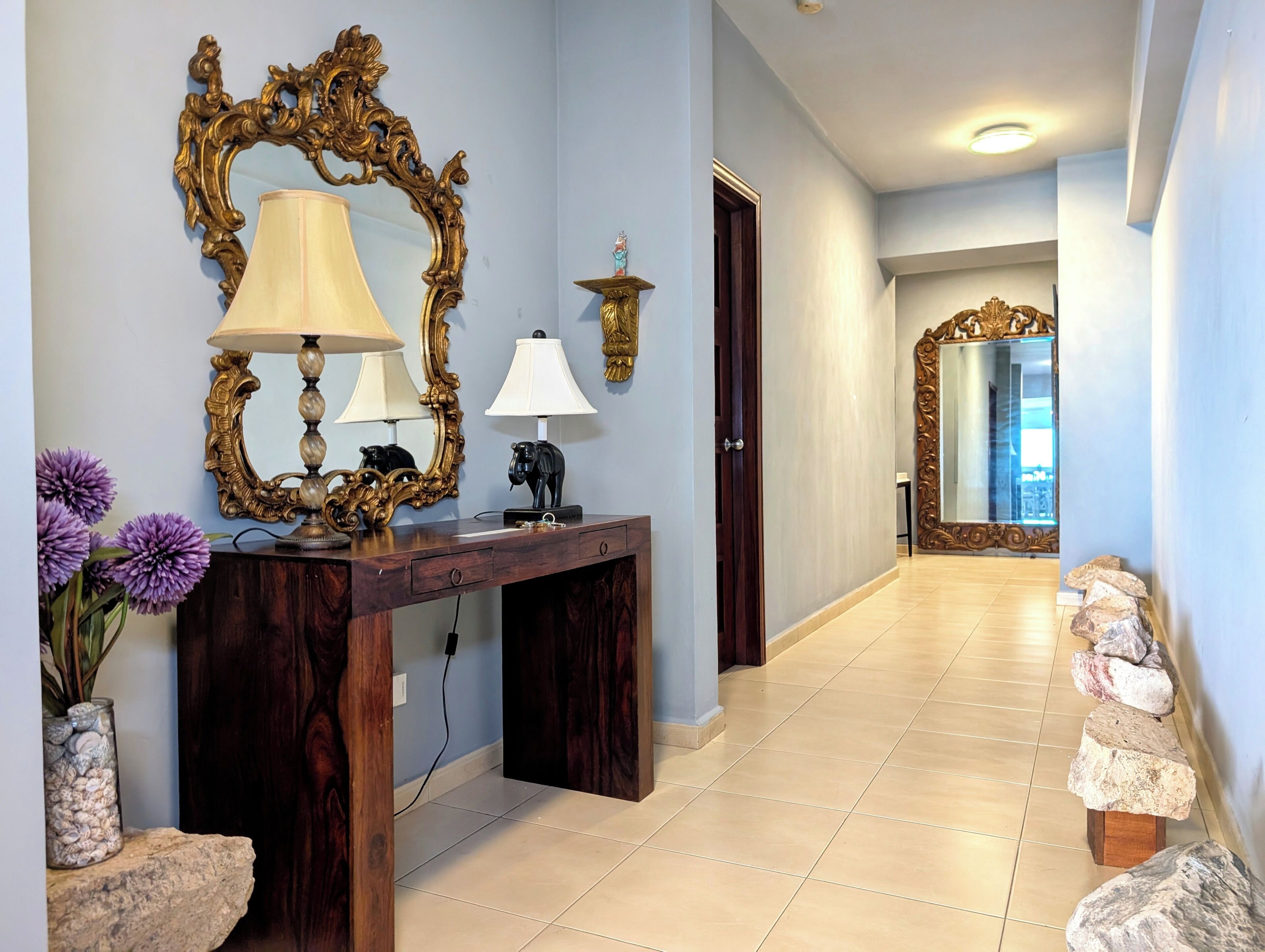 A hallway with a wooden console table, two lamps, a mirror, and a vase with purple flowers.