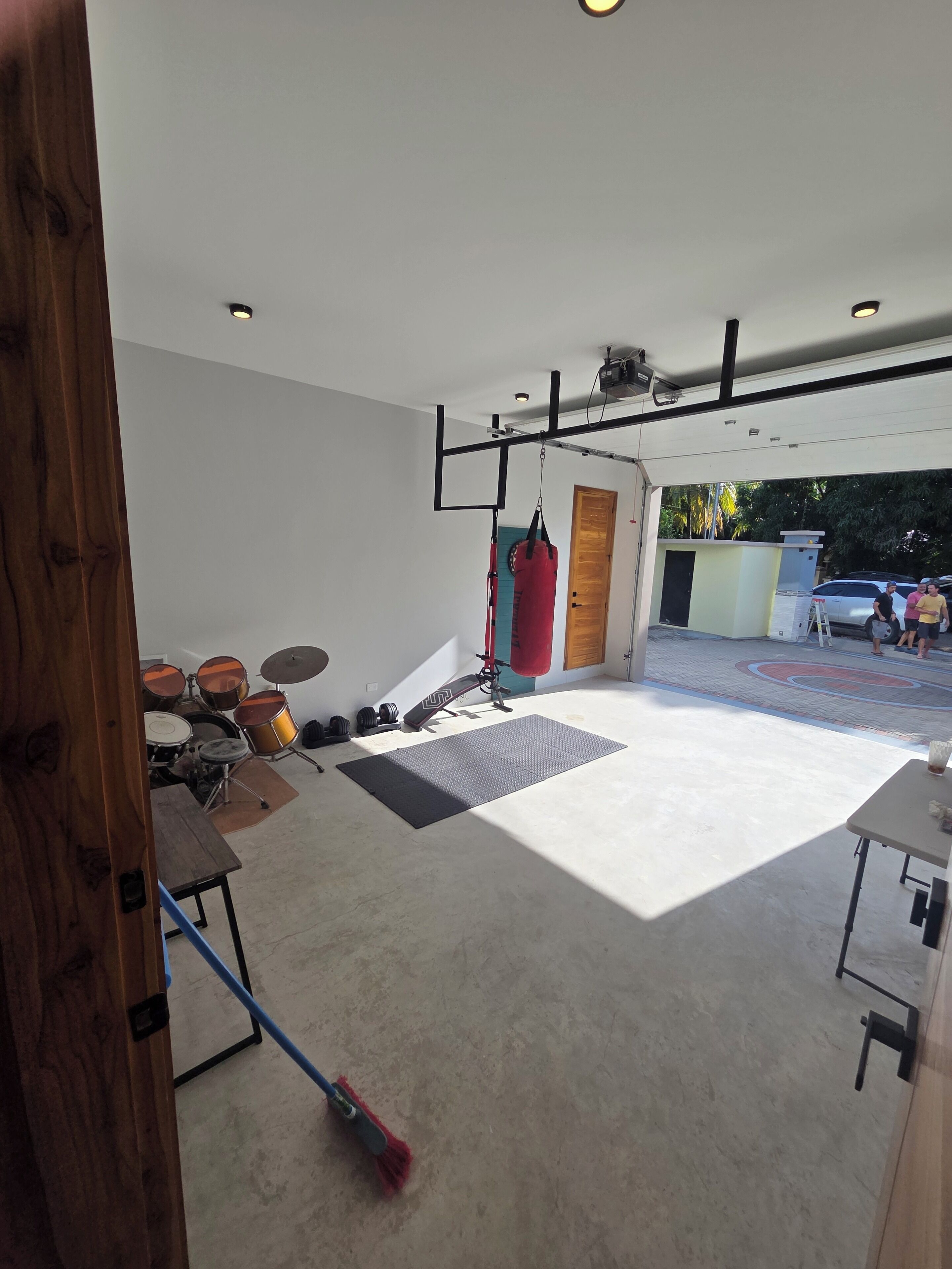 A spacious room with a concrete floor, a wooden door, a red punching bag, and a drum set.