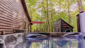 Un bain à remous avec un chalet en rondins de bois et un petit bâtiment situé dans une zone boisée.