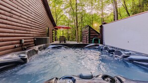 Un espace avec un bain à remous, des murs en bois, une table avec des chaises et une vue sur les arbres.