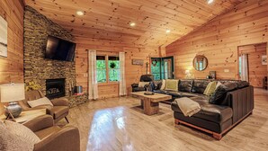 L’intérieur d’une cabane en rondins, avec une cheminée en pierre, des canapés en cuir, des planchers en bois et un téléviseur à écran plat fixé au mur.
