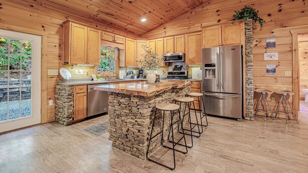 Une cuisine rustique aménagée dans une cabane en bois, avec des éléments en pierre, des appareils en acier inoxydable et un grand îlot central doté de tabourets de bar.