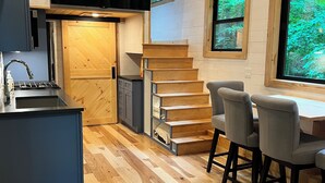 Une cuisine moderne dotée d’une cuisinière intégrée, d’un grand téléviseur à écran plat et d’un escalier en bois menant à un coin repas avec deux chaises.