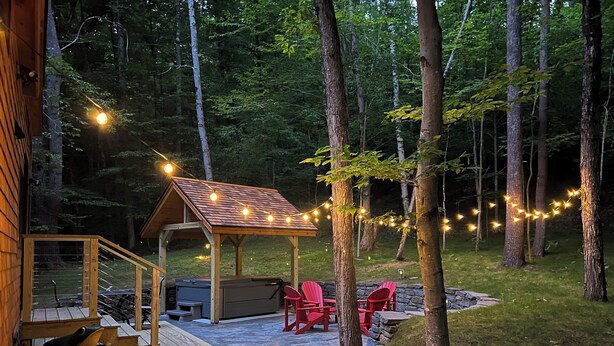 Une terrasse en bois dotée d’un espace salon couvert, d’un barbecue et de guirlandes lumineuses.