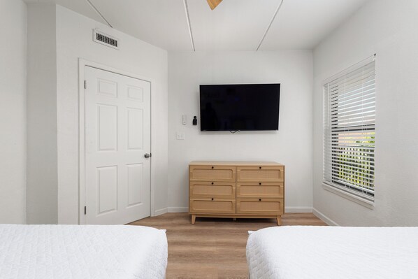 A bedroom with two beds, a TV, a wooden dresser, and a window with blinds. - On the beach - Modern Luxury condo - Ocean & Pool Views (South Padre Island)