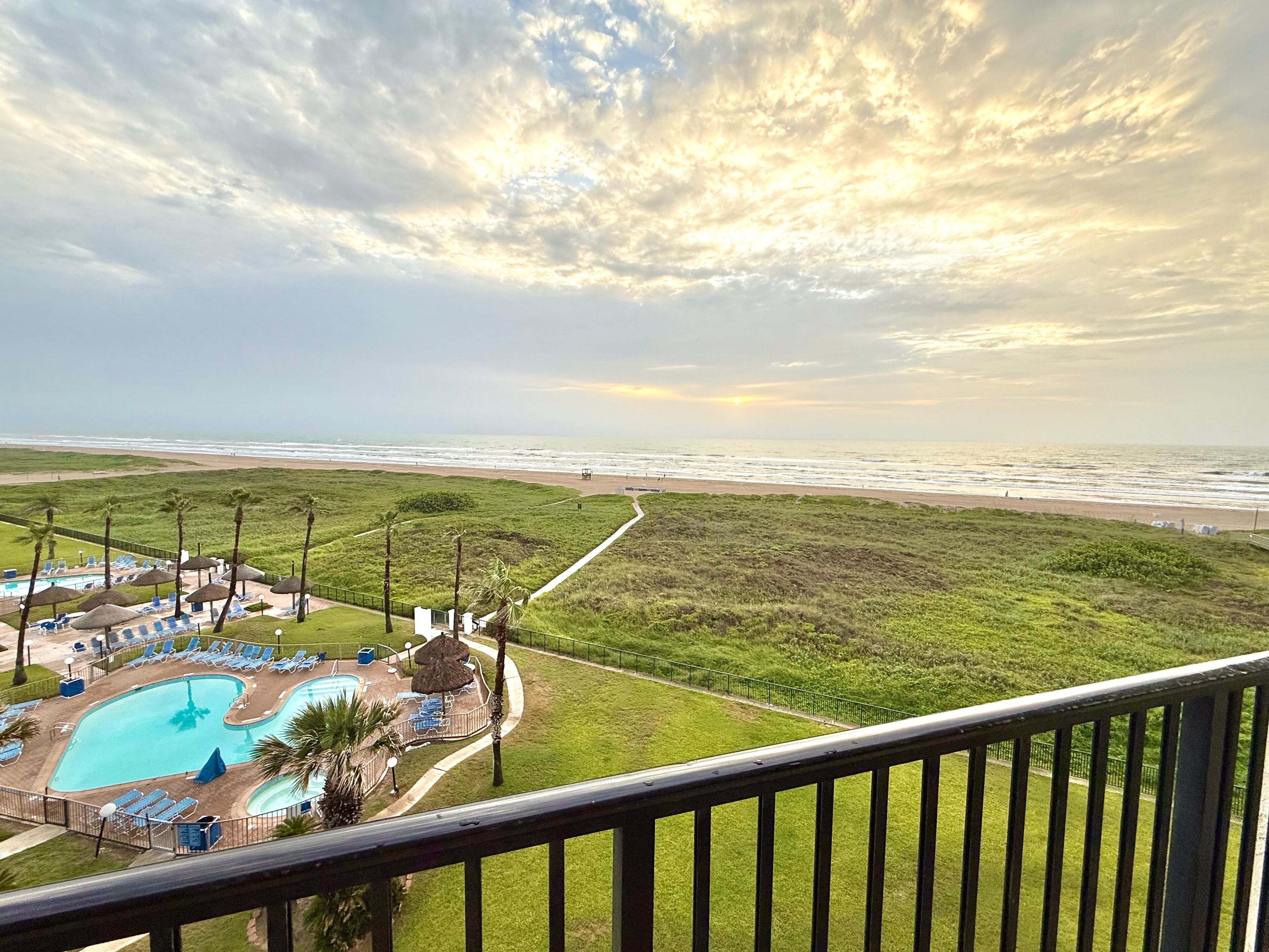 A view of a beach resort with a swimming pool, lounge chairs, and a walking path.