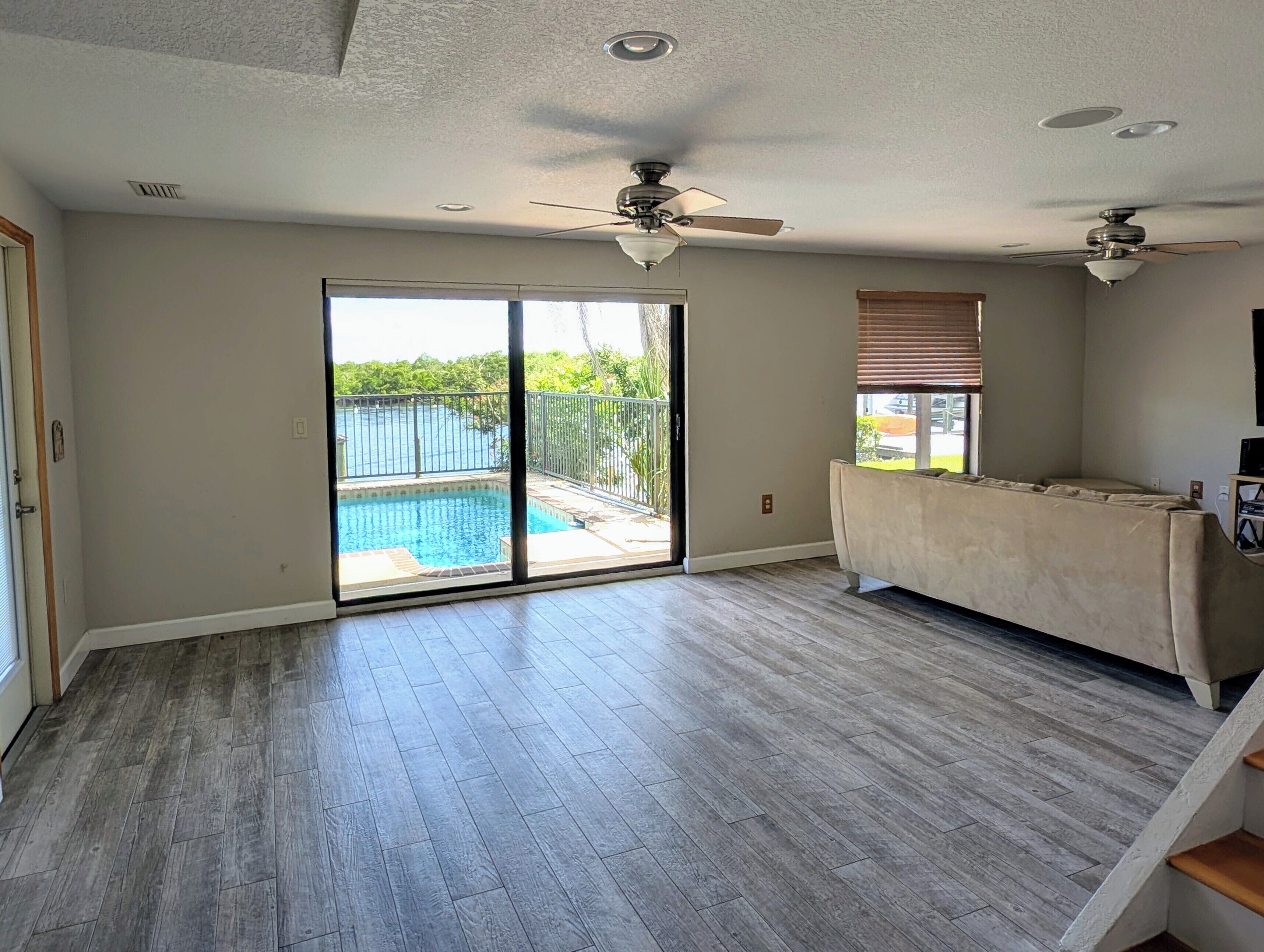 A spacious room with a large sliding glass door leading to a balcony with a pool. There are ceiling fans and recessed lighting.