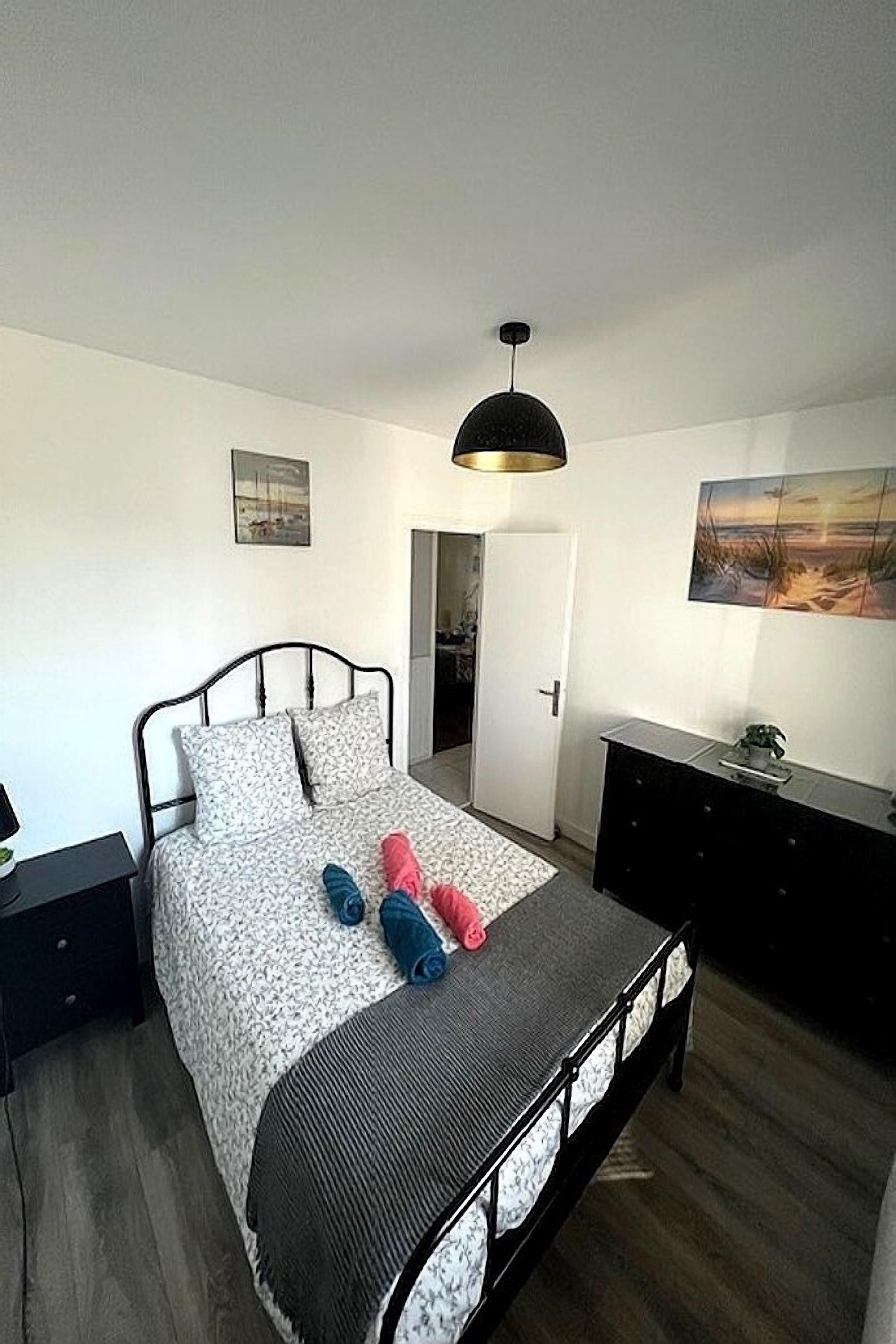 A bedroom with a bed, a nightstand, a dresser, and a hanging light fixture.
