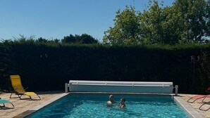 Ein rechteckiger Swimmingpool mit Sicherheitsabdeckung, umgeben von einer gefliesten Terrasse.