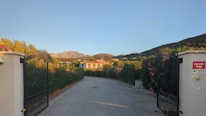 A gated driveway leading to a building with a mountainous backdrop. - Villas Maristella, spacious and comfortable Oriente 2 steps from the beach! (Aregno)