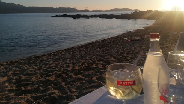 A beach with a table set for a meal, featuring a bottle and a glass labeled "MATTEI". - Villas Maristella, spacious and comfortable Oriente 2 steps from the beach! (Aregno)