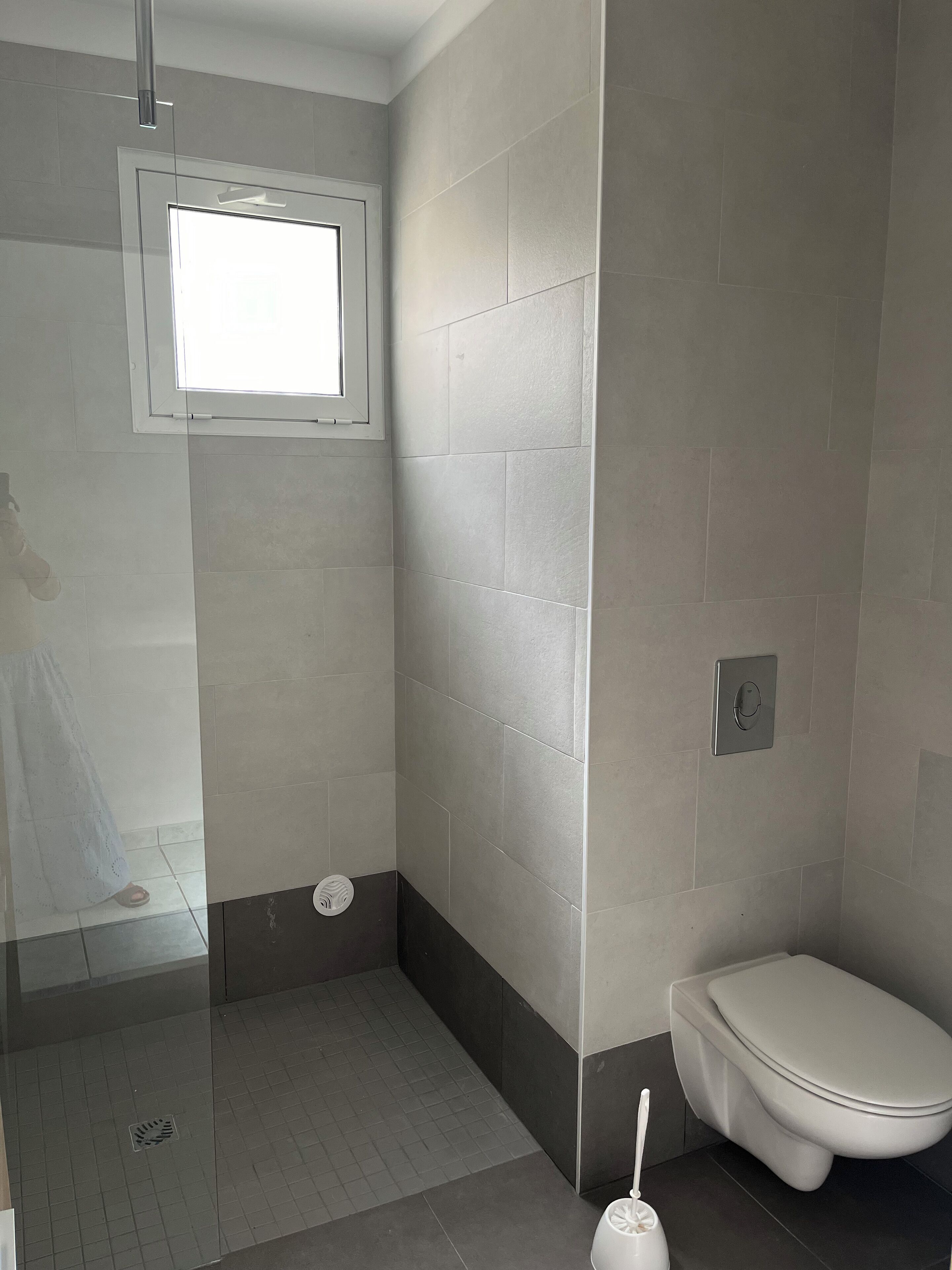 A bathroom with a shower, toilet, and a window.