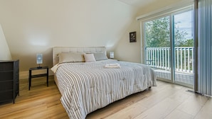 Una camera da letto con un letto grande, un comodino, una cassettiera e un balcone con vista sugli alberi.