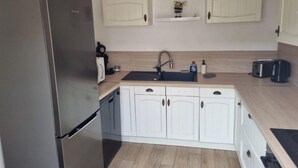 A modern kitchen with white cabinets, a stainless steel refrigerator, a sink, and a coffee maker.