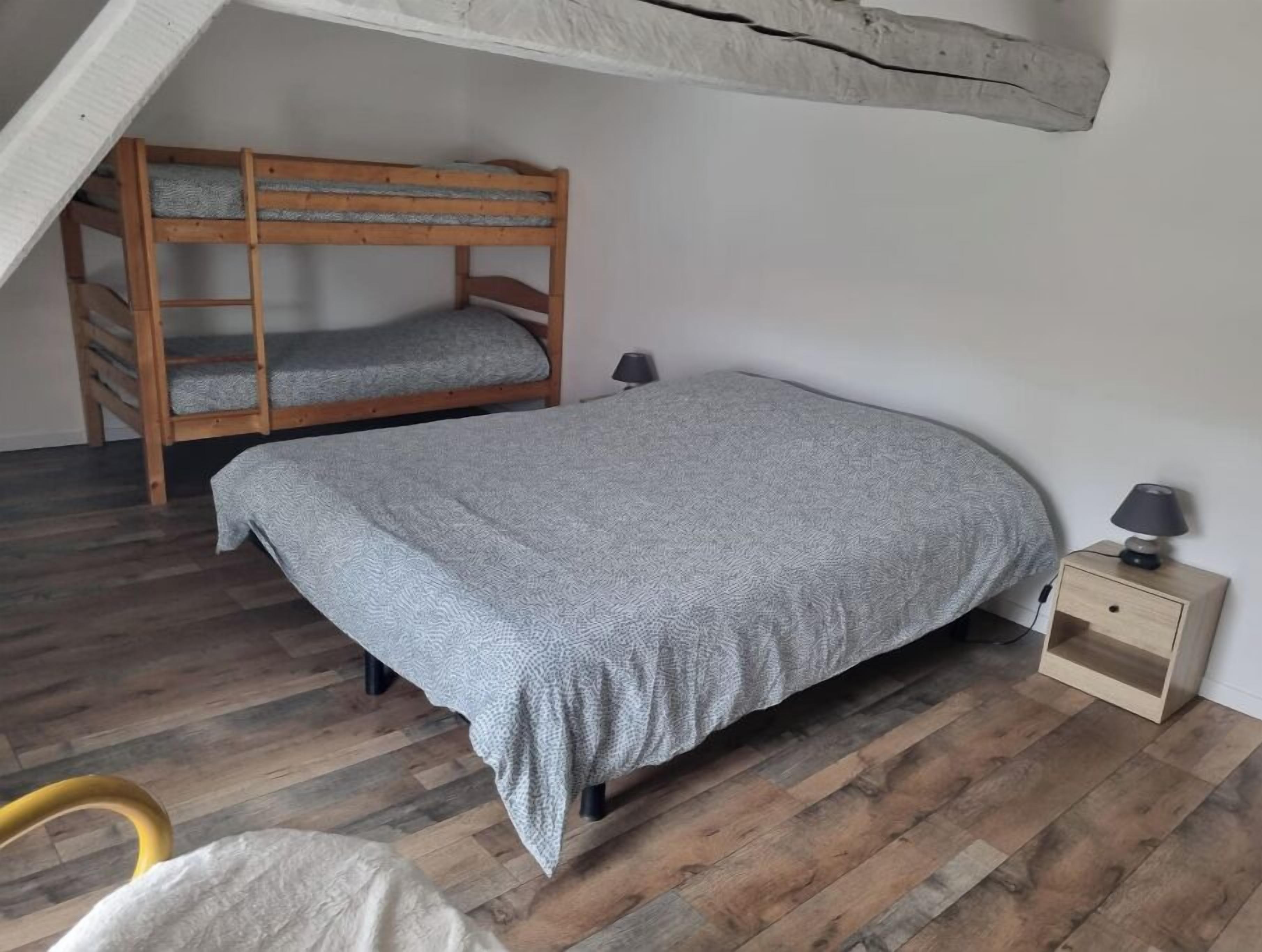 Et soveværelse med køjeseng, enkeltseng, natbord med lampe og en stol.