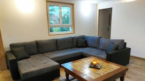 A living room with a sectional sofa, a wooden coffee table, and a window with a view of trees.