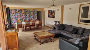 A living room with a grey sofa, wooden coffee table, dining area with chairs and a table, and a colorful abstract wall.