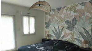 A bedroom with a bed, a window, a wall with a leaf pattern, and a hanging light fixture.