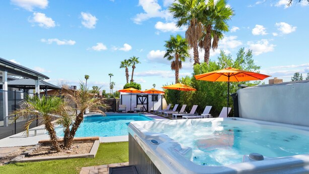 Een zwembad met ligbedden en parasols, een jacuzzi en palmbomen.