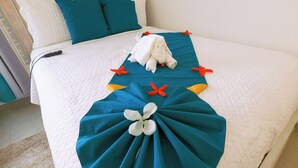 Un lit bien fait, avec une couette blanche, des éléments décoratifs aux tons turquoise et bleu, et un animal en peluche blanc.