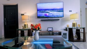 Un salon moderne avec une table basse en verre, un téléviseur à écran plat et deux lampes.