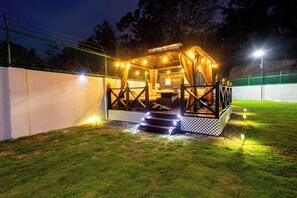 Un espacio al aire libre bien iluminado con una terraza de madera y escalones que llevan a ella, rodeado por una cerca y un área con césped.
