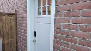 A white door with a small window, a wooden gate, and a brick wall. - Cozy 2-Bedroom Basement Apartment In Toronto (Toronto)