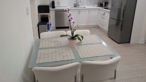 A modern kitchen with white cabinets, a stainless steel refrigerator, and a dining table with placemats. - Cozy 2-Bedroom Basement Apartment In Toronto (Toronto)