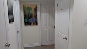 A hallway with white doors, a painting on the wall, and a ceiling light. - Cozy 2-Bedroom Basement Apartment In Toronto (Toronto)