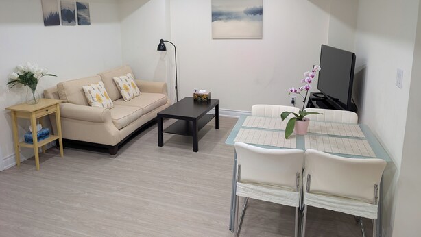 A living room with a sofa, coffee table, TV, and a dining area with chairs and a table. - Cozy 2-Bedroom Basement Apartment In Toronto (Toronto)