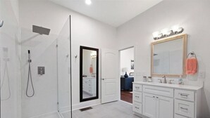 A modern bathroom with a walk-in shower, a vanity with a large mirror, and a door leading to another room. - Historic Downtown Studio (Pensacola)
