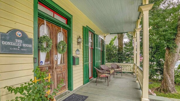 A porch with green shutters, a sign reading "The Gonzalez House circa 1880", and wicker chairs. - Historic Downtown Studio (Pensacola)