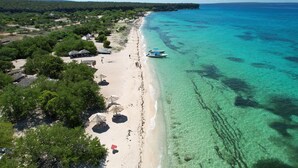 An aerial view of a beach with clear turquoise waters, a sandy shore, and several thatched-roof huts. - Hotel Casa Bajari (Pedernales)
